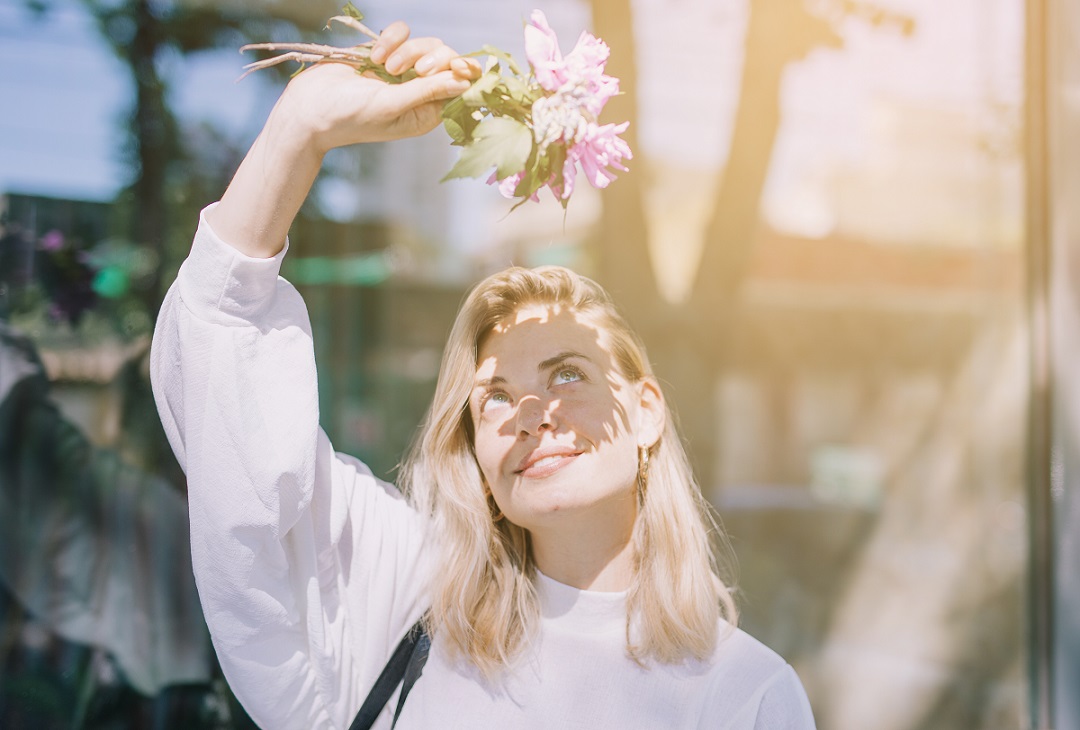 Mujer joven rubia que sostiene flores que protege su cara y sus ojos de la luz del sol