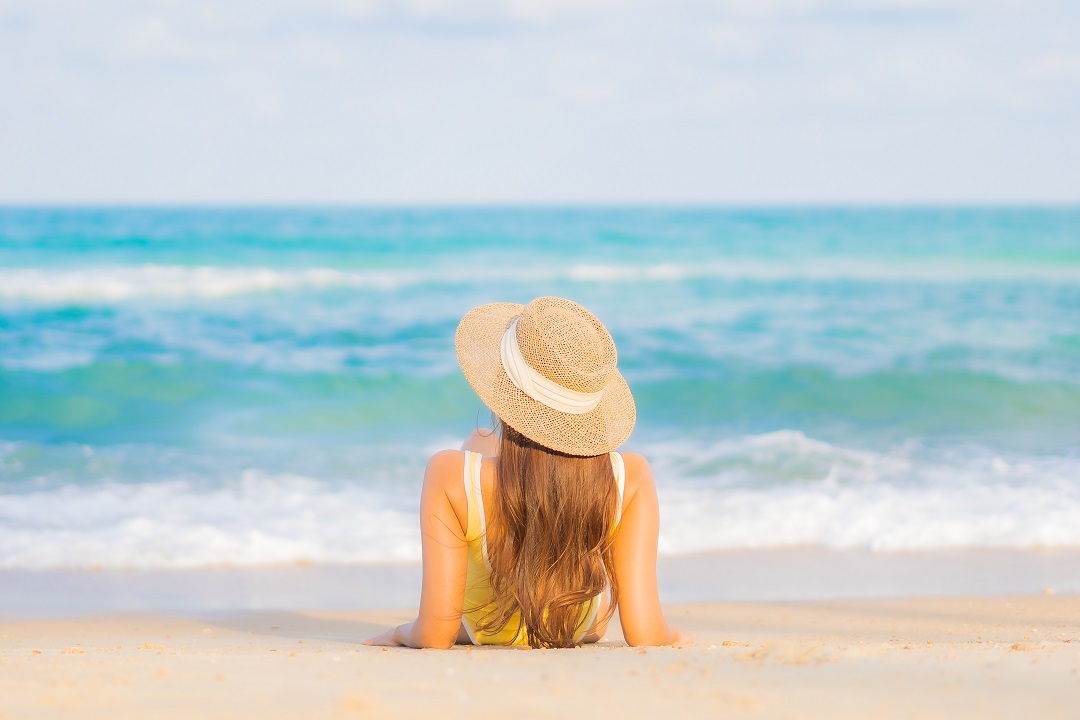 mujer joven con sombrero tomando el sol en el mar