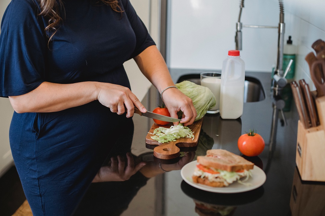 Mujer embarazada cortando verduras y preparando comida