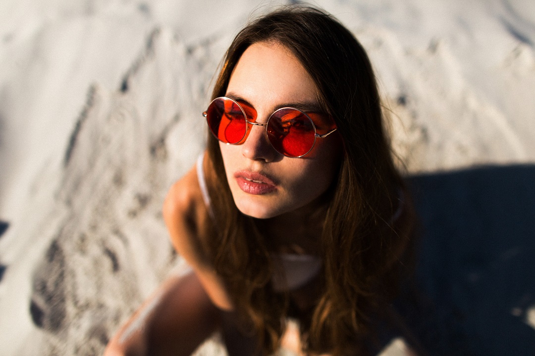 mujer pelo largo gafas sol rojas sienta arena blanca f