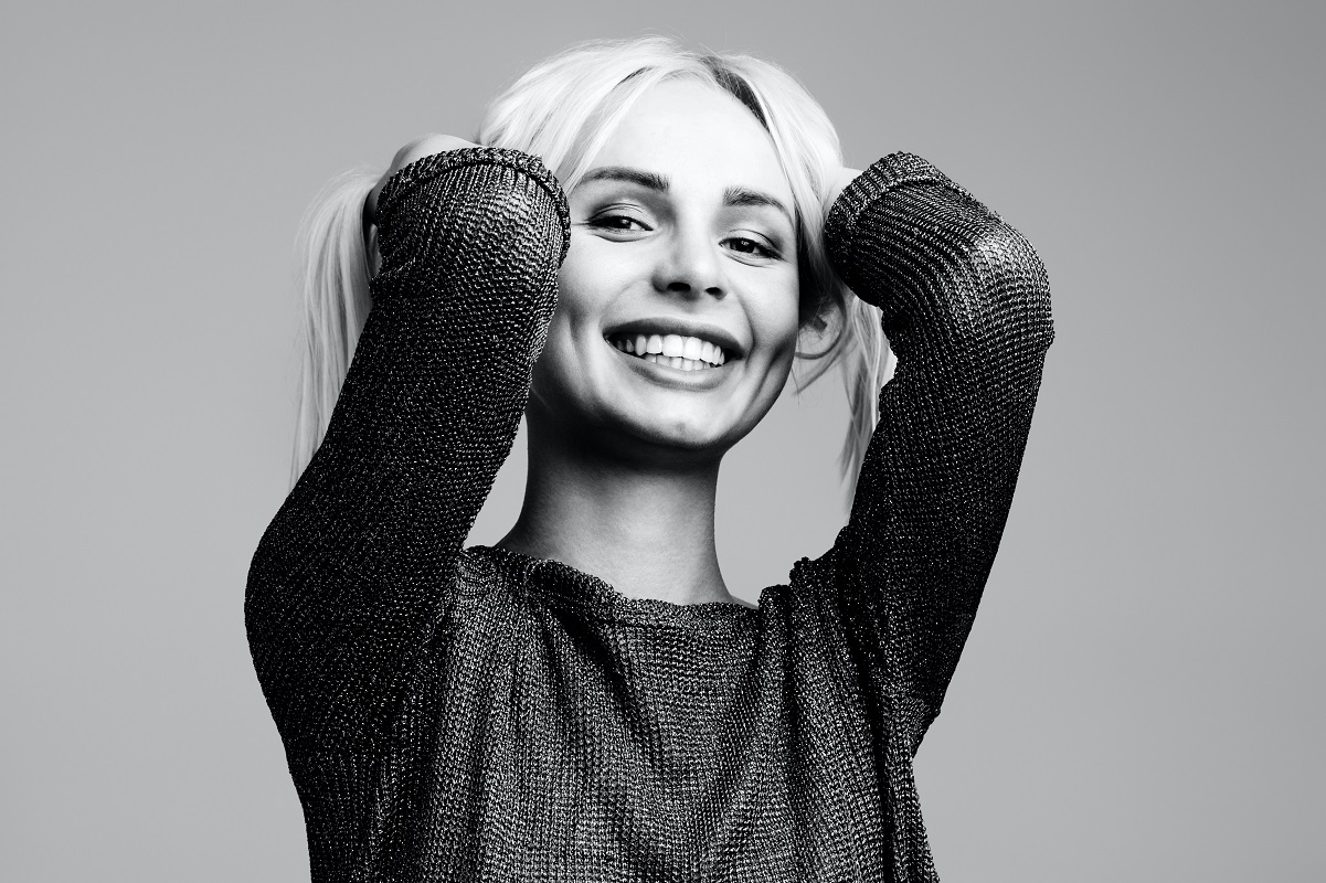 Mujer rubia con suéter sonriendo riendo agarrando su cabello