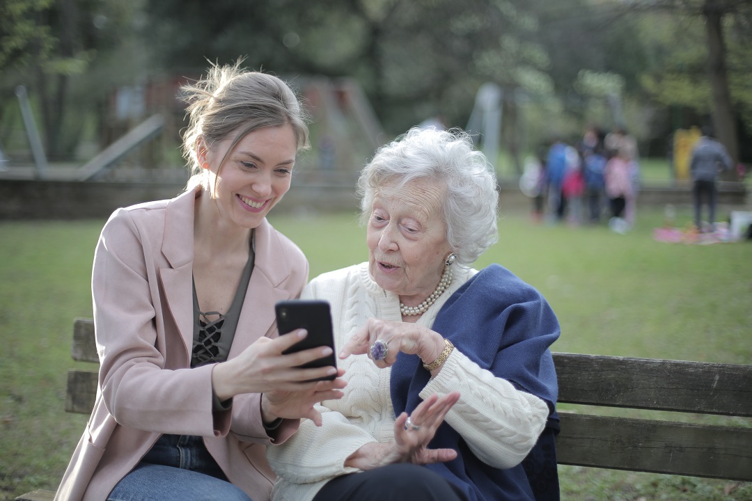 Mujer joven enseñando teléfono a mujer anciana