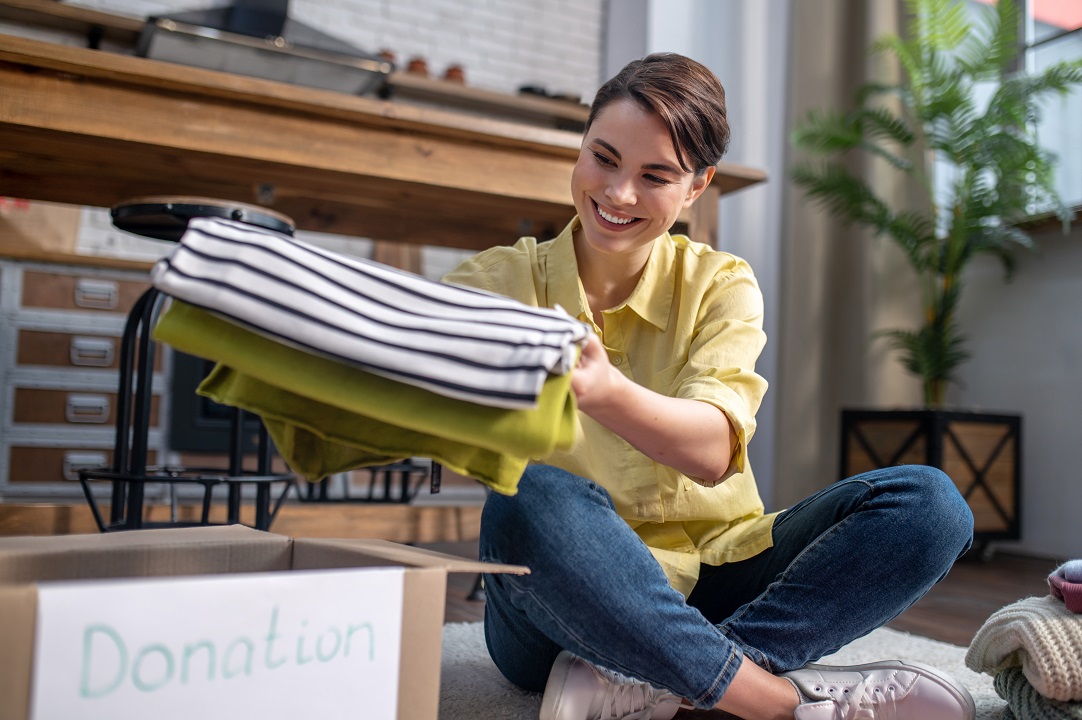 Mujer sentada en el suelo empacando ropa para donación reciclaje