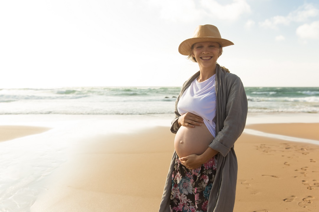 mujer embarazada feliz sonriente con las manos en el vientre playa sol