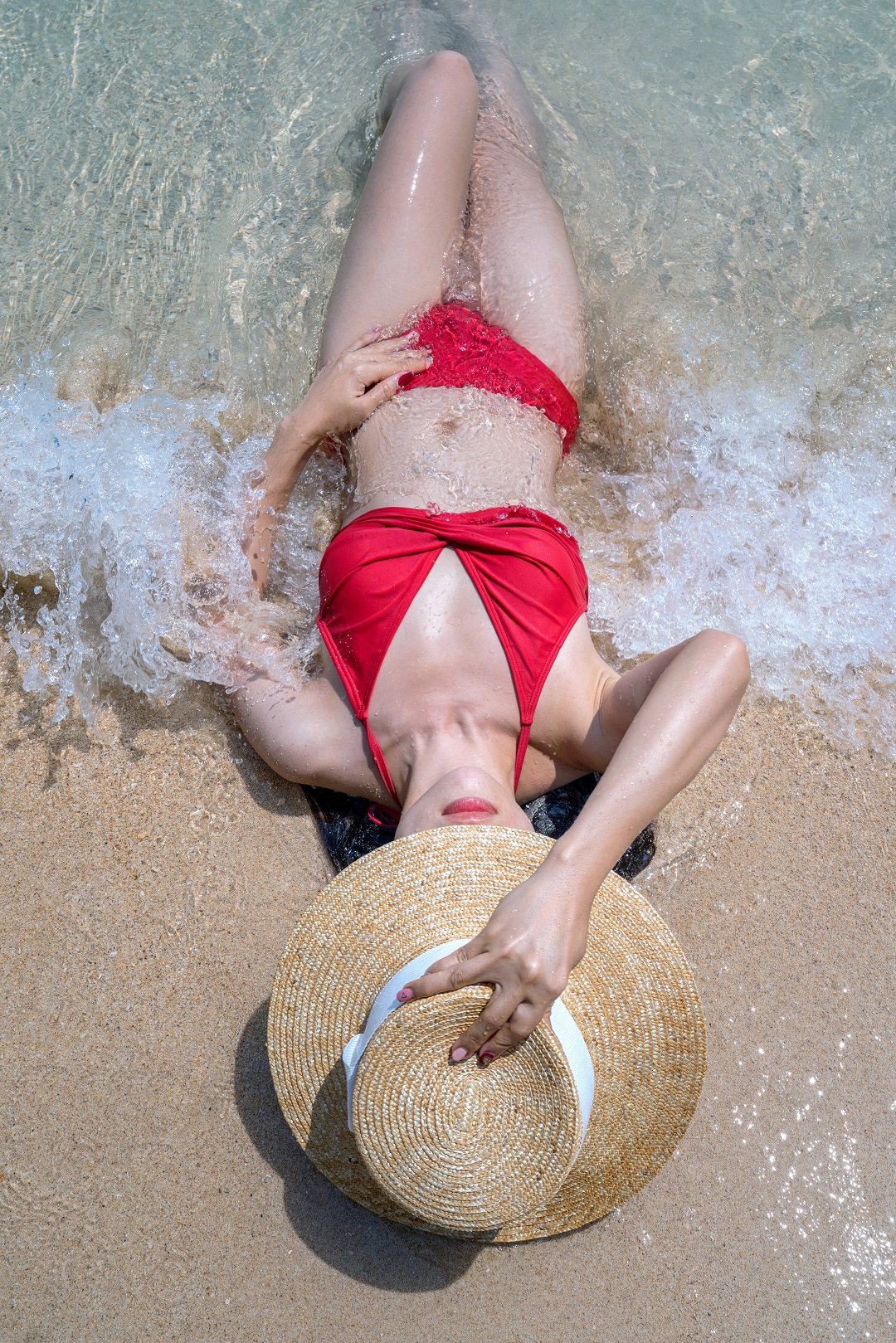 mujer acostada en playa olas mar agua bikini rojo sombrero