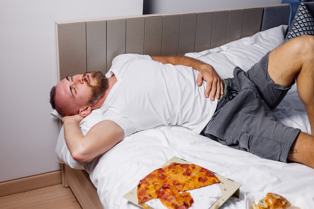Hombre barba cama pizza comida chatarra dormir malestar estomacal