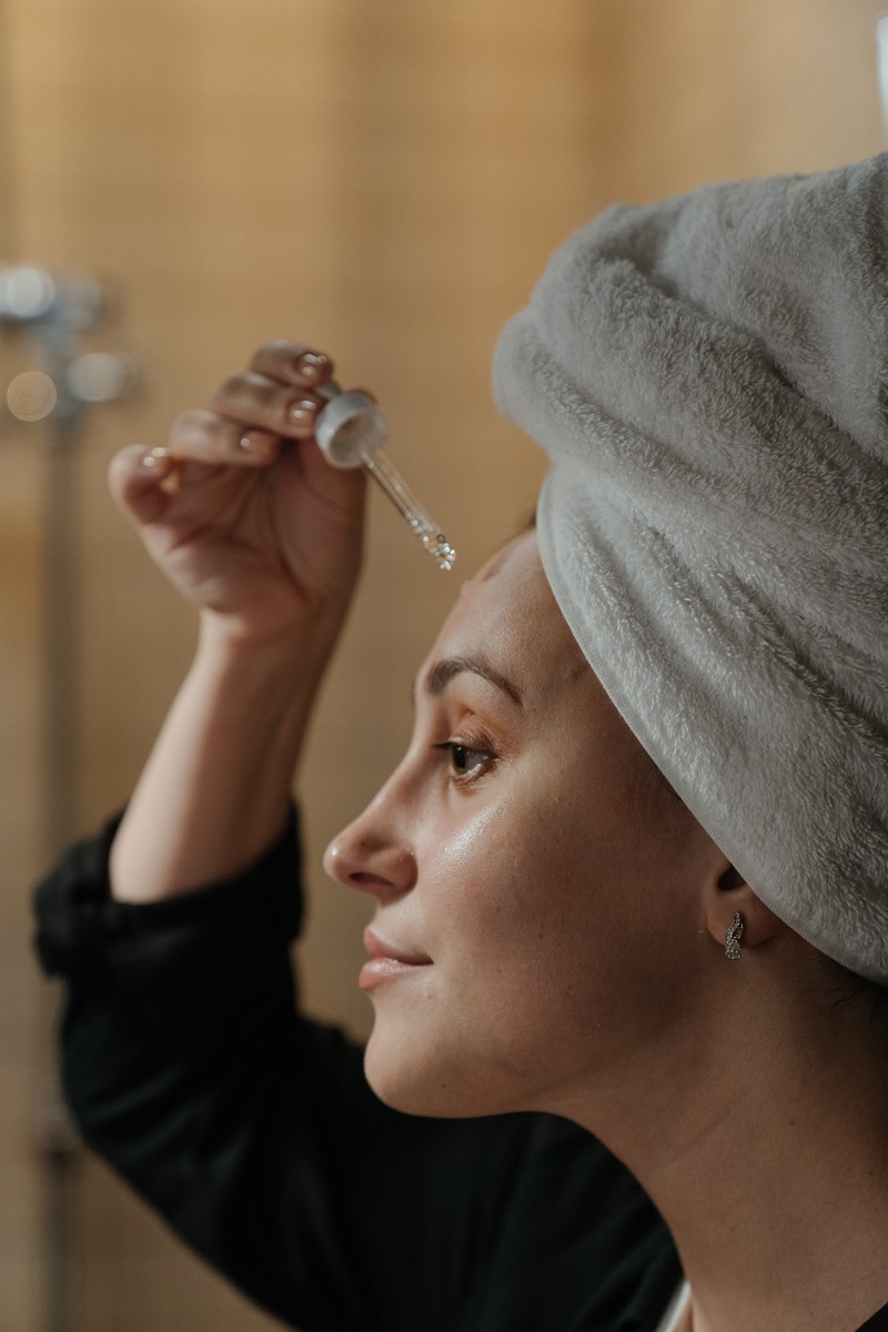 Mujer bata negra gotero vitamina C suero toalla cabeza espejo baño skincare rutina cara rostro
