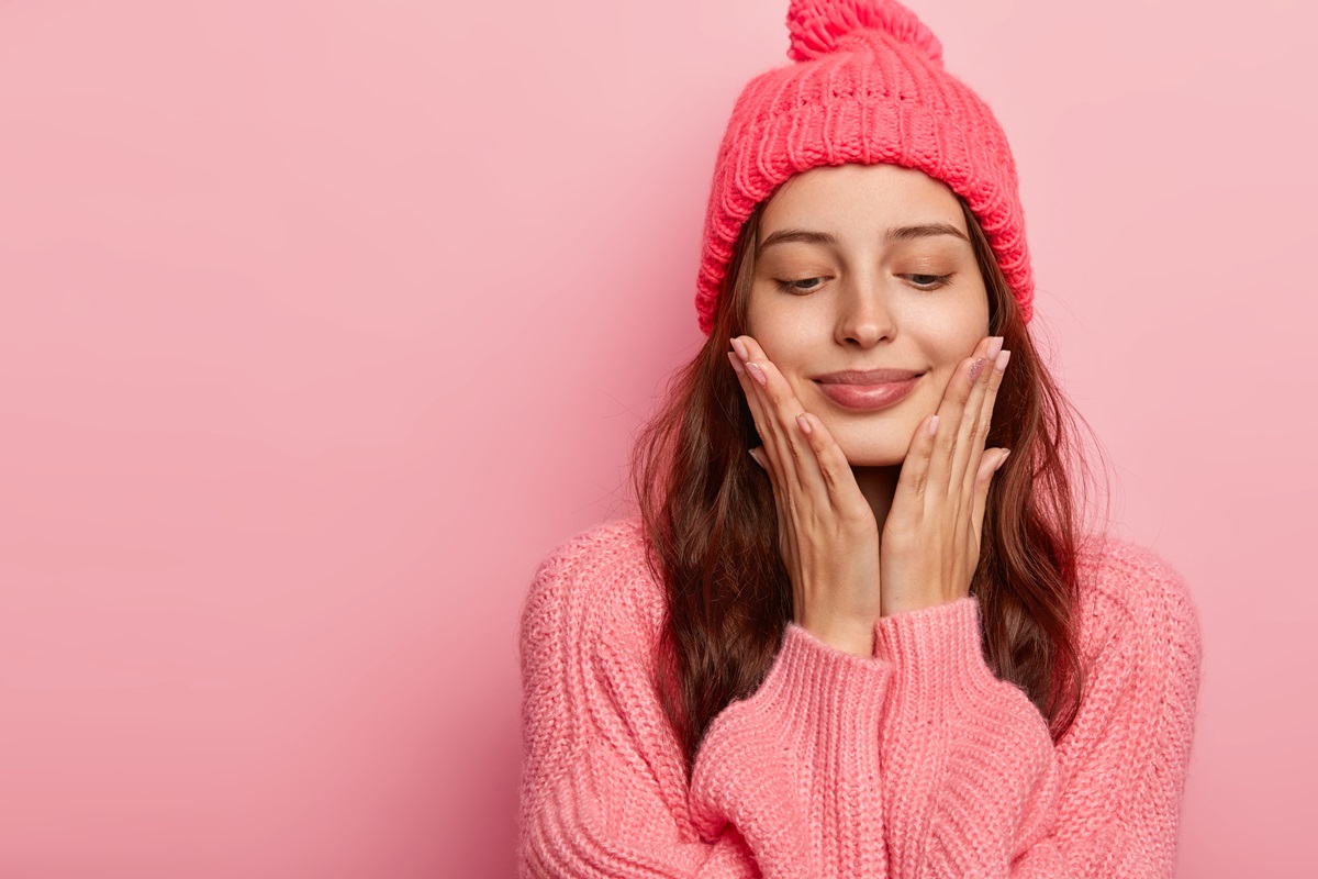 Mujer frío invierno skincare ropa abrigadora suéter gorro fondo rosa