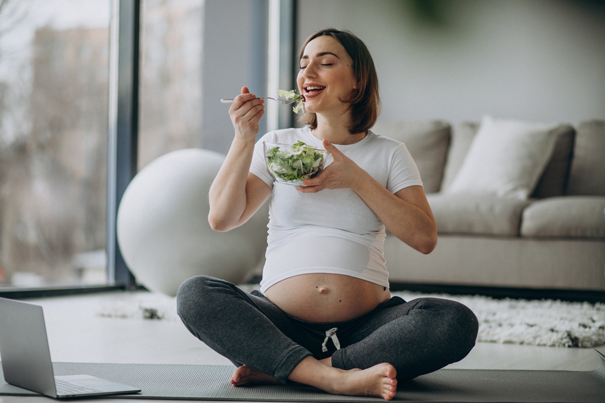 Embarazada comiendo ensalada sentada en sala casa
