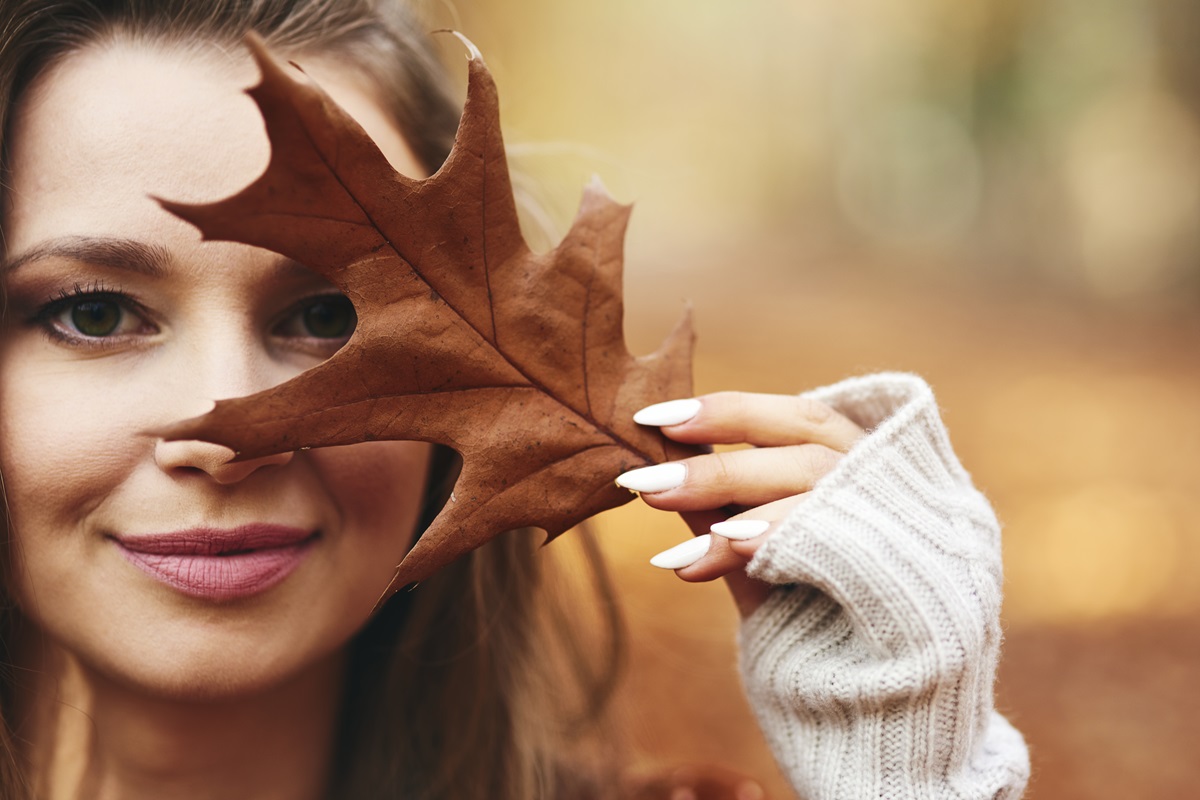 Mujer cubriendo su rostro con hoja de otoño