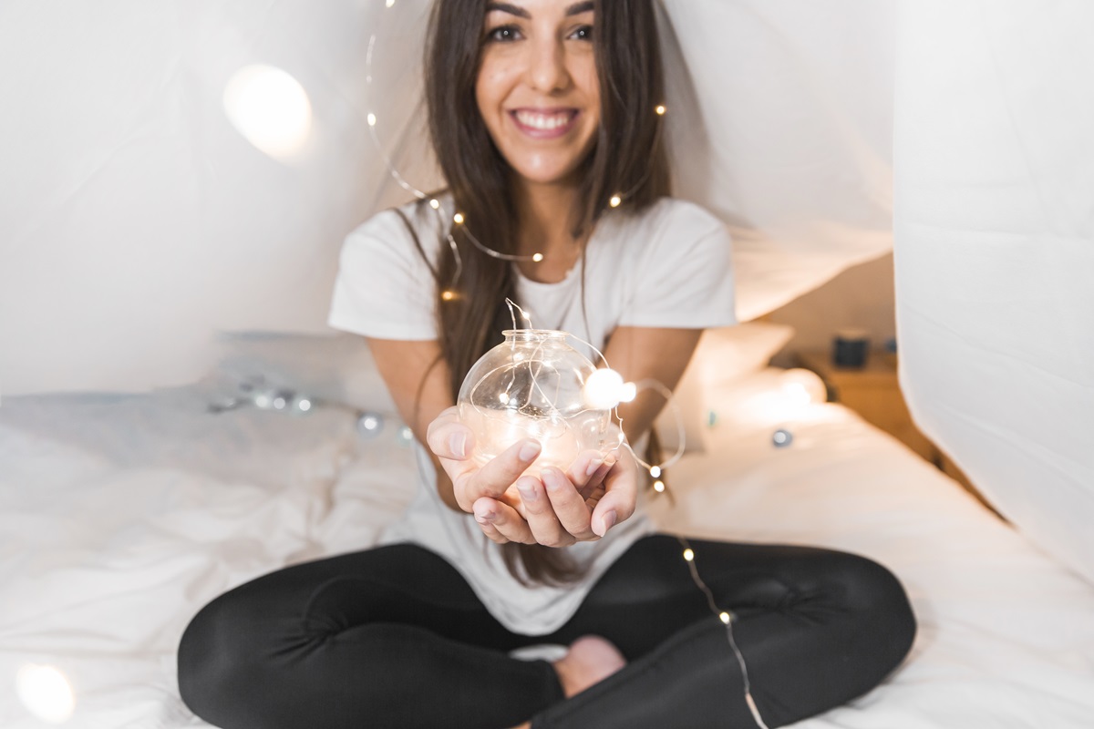 Mujer joven feliz sentada en la cama sosteniendo una esfera brillante