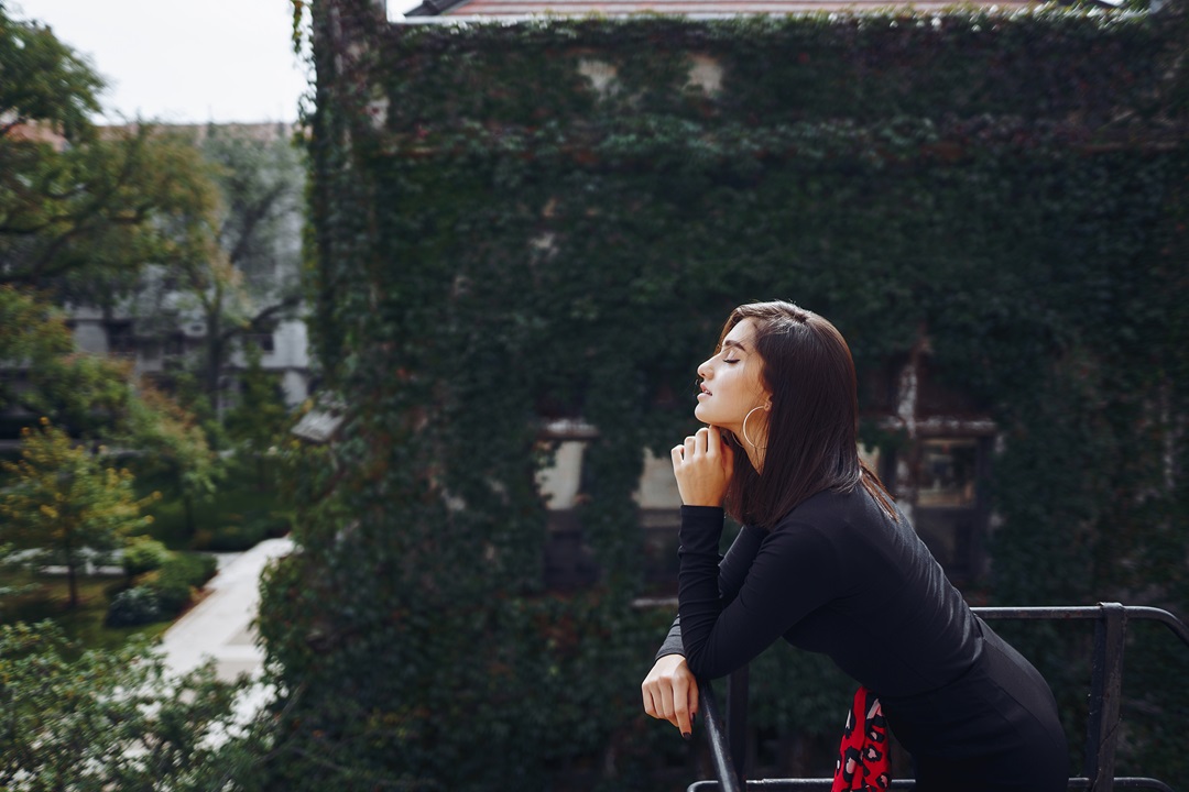 beautiful brunette posing on a staircase with breathtaking background of a building covered in ivy