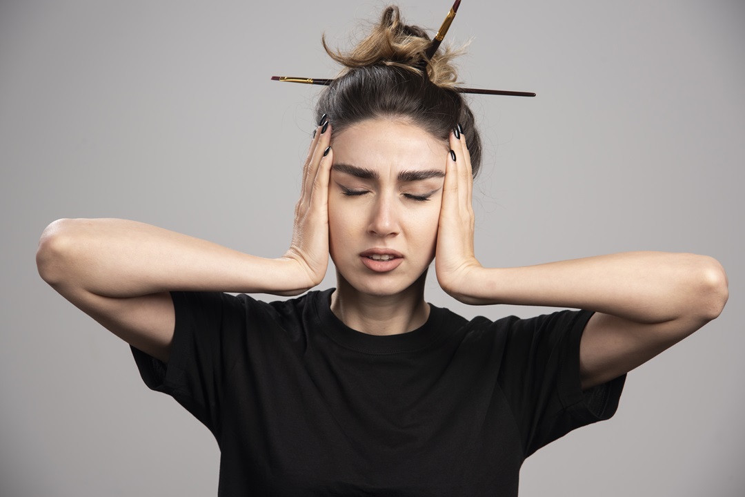 Young woman with messy bun holding her head on gray background